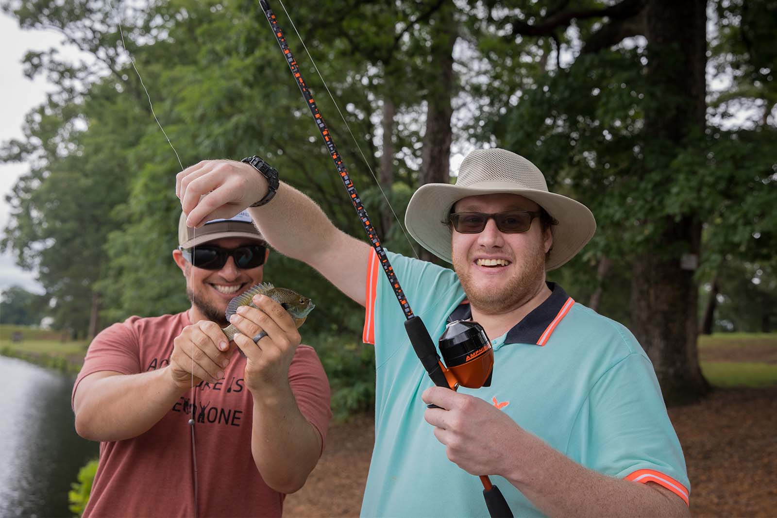 ሁለት ሰዎች በሀይቅ ዳርቻ ላይ ቆመው ነበር. አንድ ሰው የዓሣ ማጥመጃ ዘንግ ሲይዝ ሌላኛው ደግሞ ከመንጠቆው የተወገደውን ዓሣ ይይዛል