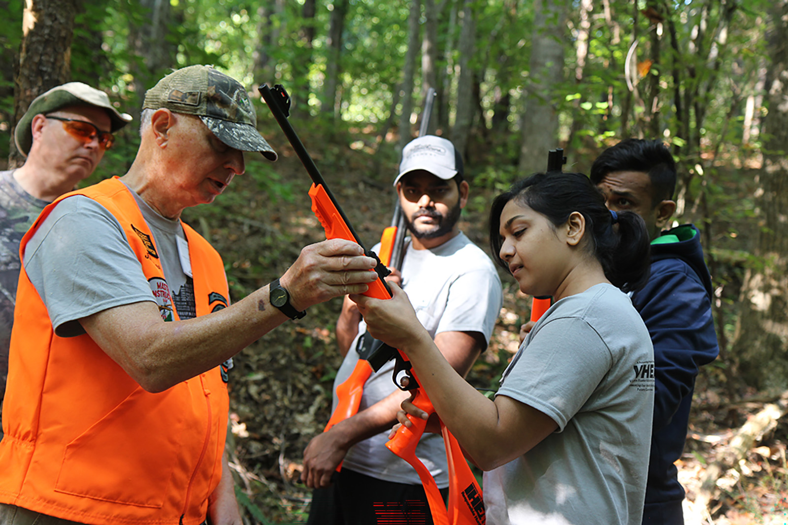 አንድ ወንድ ቡድን እያየ ሽጉጥ እንዴት ለሴት እንደሚይዝ ሲያብራራ የሚያሳይ ፎቶ።