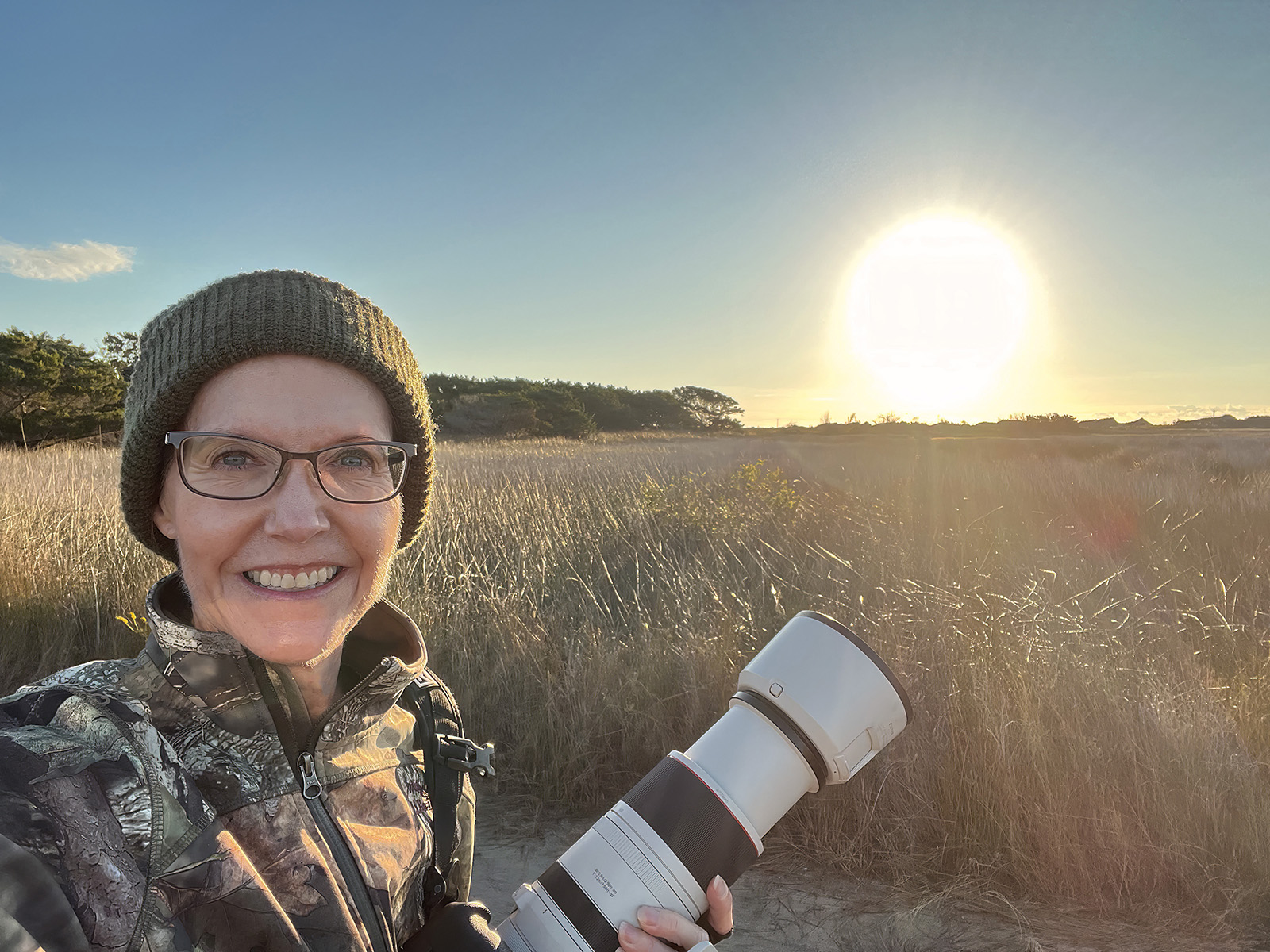 ረግረግ አጠገብ ፀሐይ ስትወጣ ካሜራ የያዘች ሴት ፎቶ።